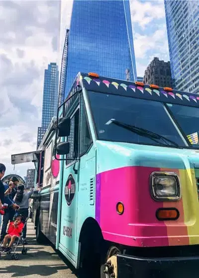A brightly colored food truck parked in front of a skyscraper in downtown New York City