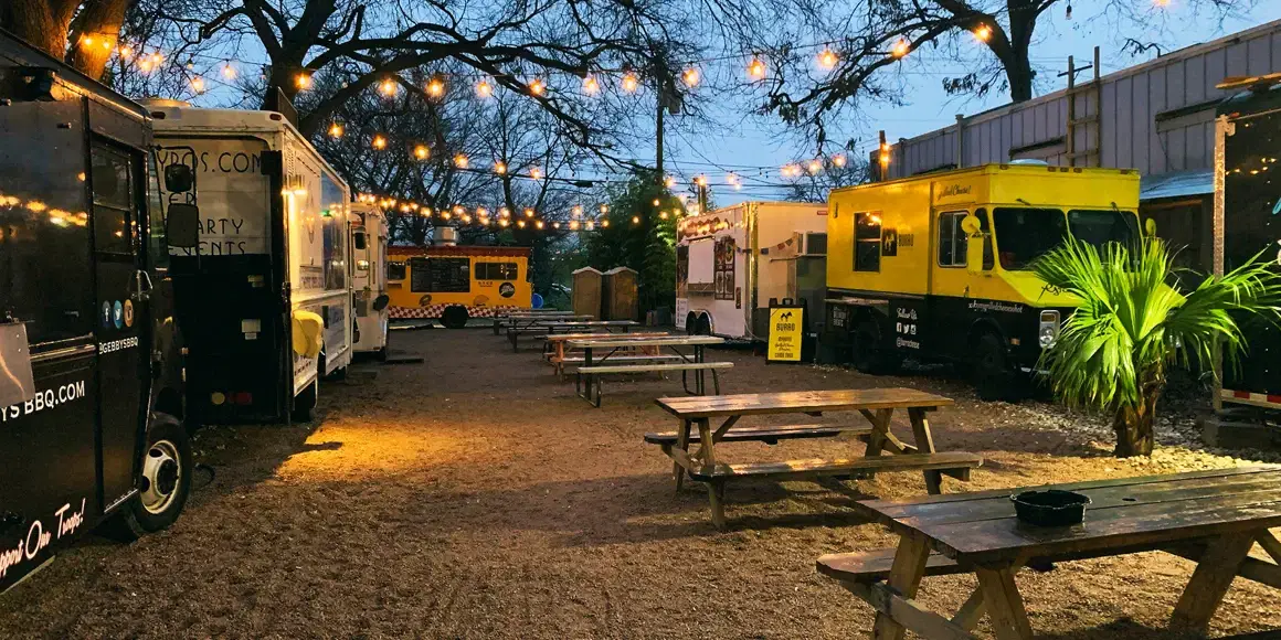 A park with food trucks, picnic tables, and string lights
